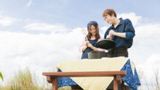 青空の下で料理をする若い夫婦の画像