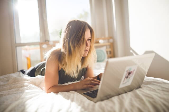 ベッドの上でパソコンを操作する女性の画像